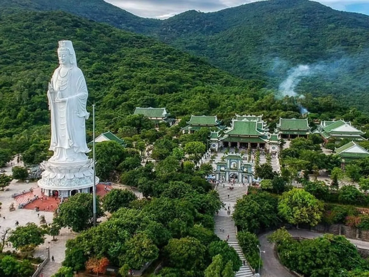 Close aerial view of the Lady Buddha statue at Linh Ung Pagoda Da Nang showing the full 20-hectare temple complex with green-roofed buildings, courtyard and Son Tra mountain forest