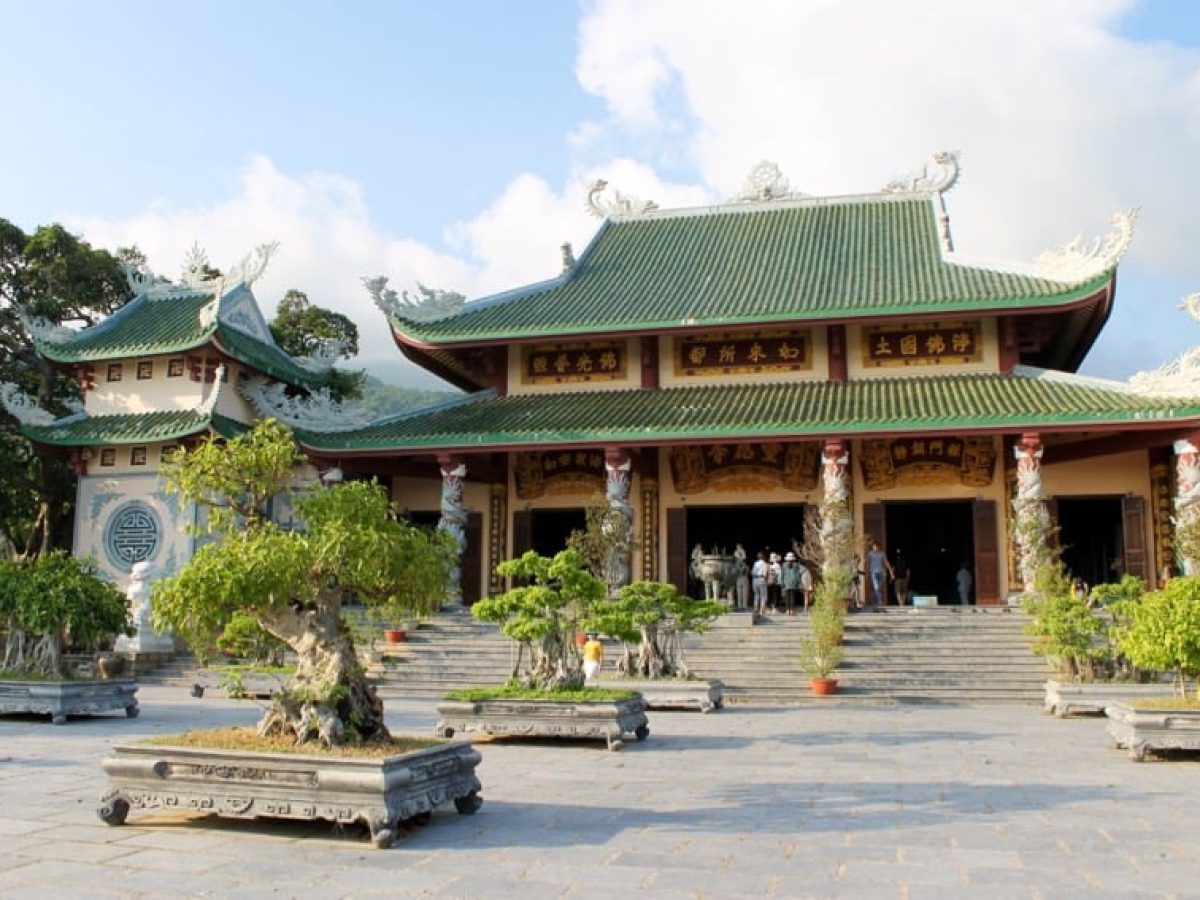 The main worship hall Chanh Dien of Linh Ung Pagoda Da Nang with three-tiered green glazed roof, ornate dragon columns and ancient bonsai garden in the foreground
