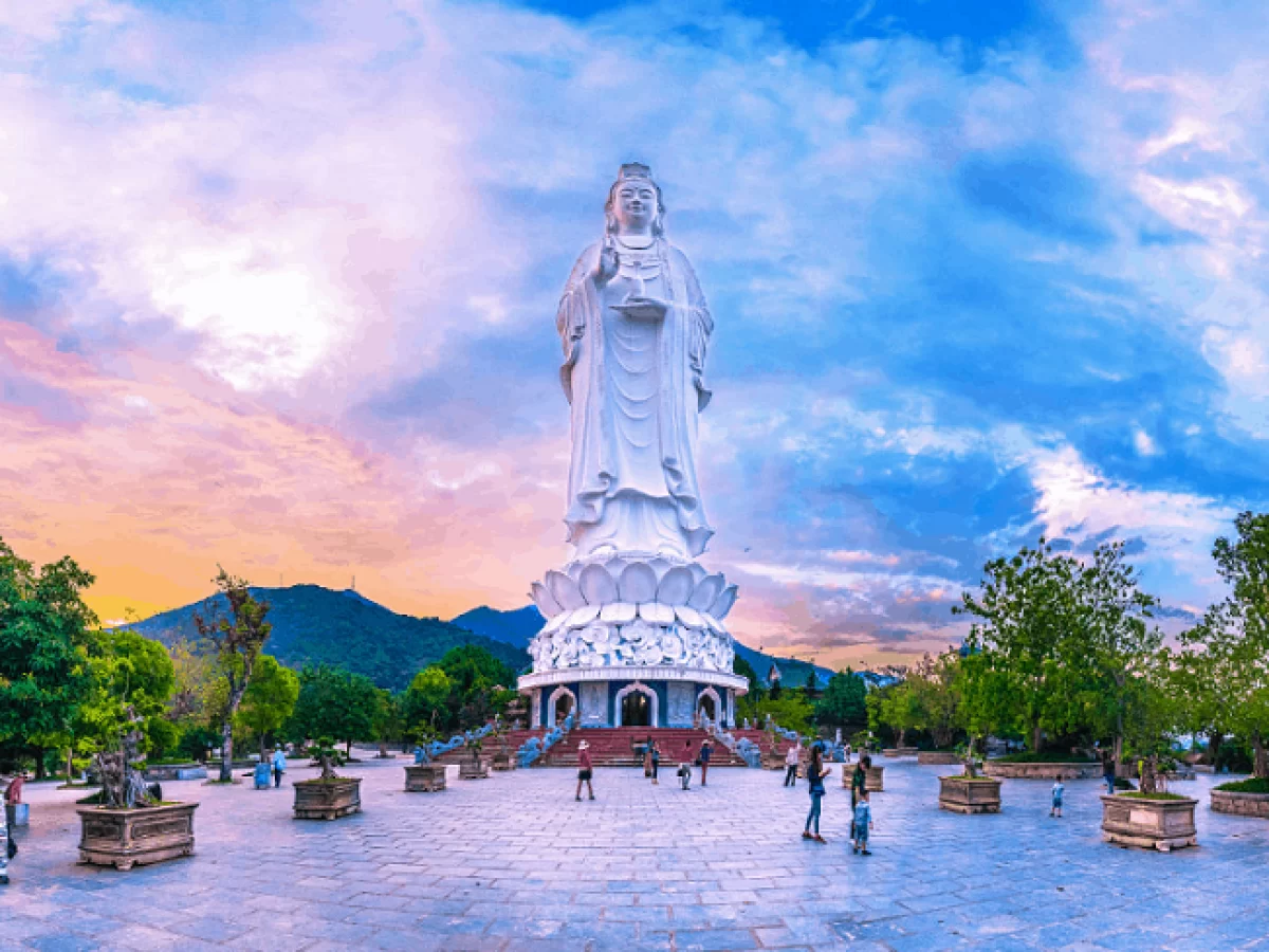 The 67-metre Lady Buddha statue at Linh Ung Pagoda Da Nang photographed at sunset with colourful sky, lotus base and temple courtyard with visitors in foreground