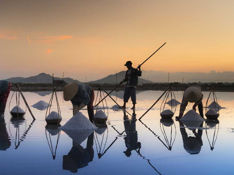 Hon Khoi Salt Fields near Nha Trang — Vietnam Discovery Tours Salt farmers harvesting sea salt at Hon Khoi salt fields near Nha Trang at sunset, a traditional craft village near the bay islands