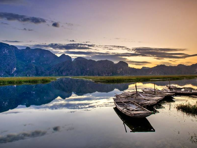 Wooden boats moored on still water at sunset in Van Long Nature Reserve