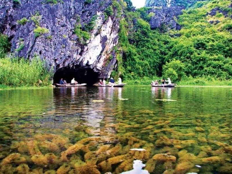 Visitors on small boats passing through a limestone cave at Van Long Nature Reserve