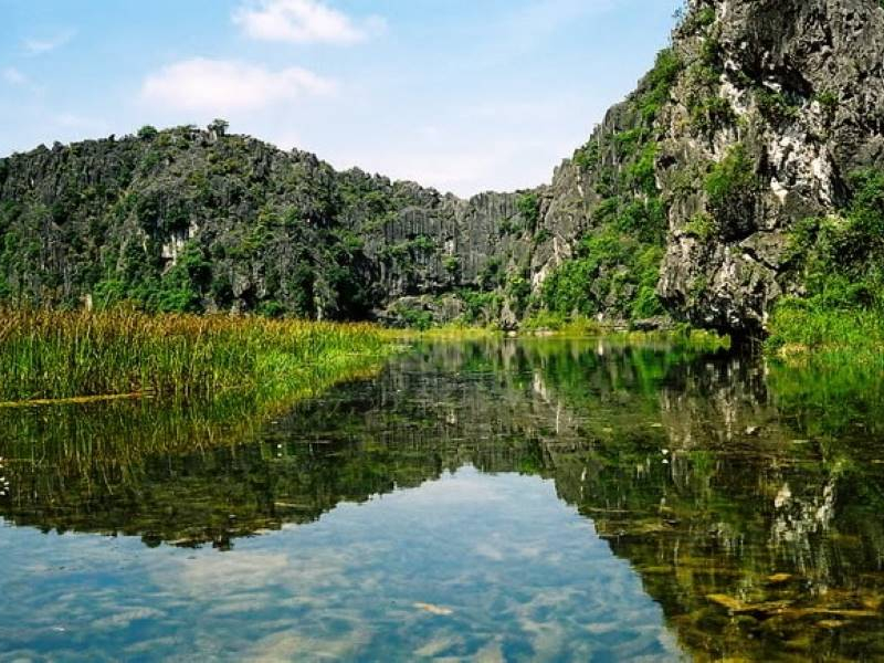 Limestone karst mountains reflected in the calm wetland waters of Van Long Nature Reserve
