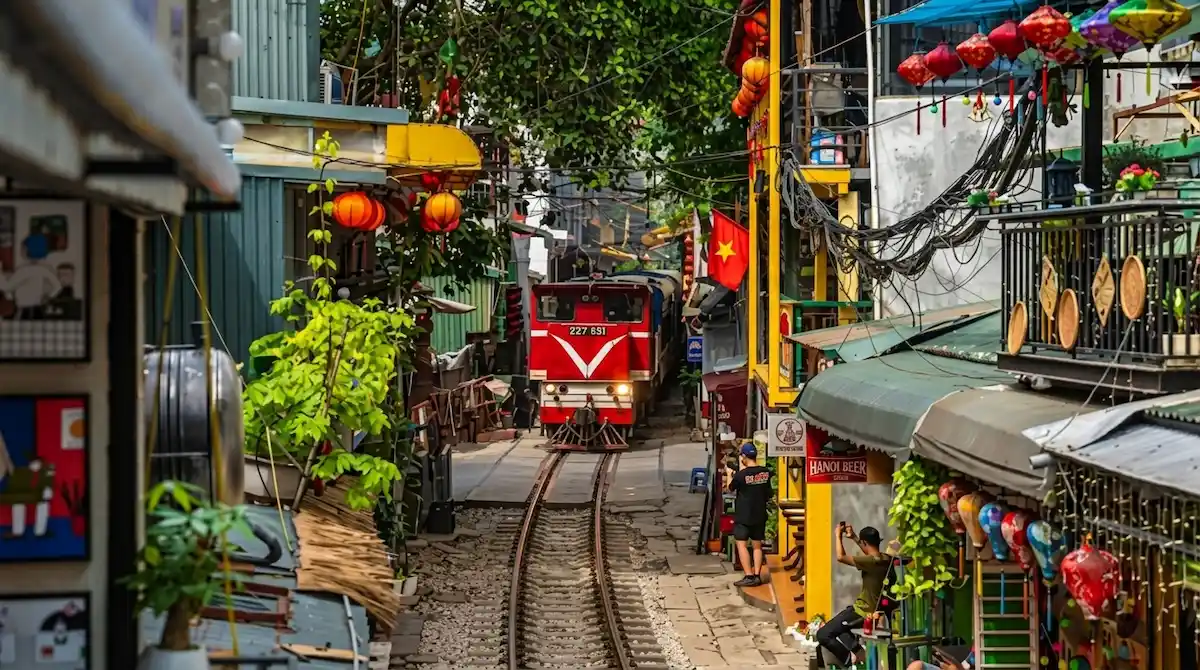 Red train passing through narrow Hanoi Train Street surrounded by local cafes and lanterns