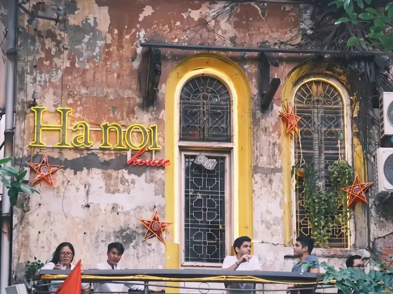 Hanoi House Cafe Balcony and Vintage Facade - Vietnam Discovery Tours Weathered vintage facade with glowing neon sign and guests relaxing on the balcony at Hanoi House Cafe near St. Joseph's Cathedral Hanoi