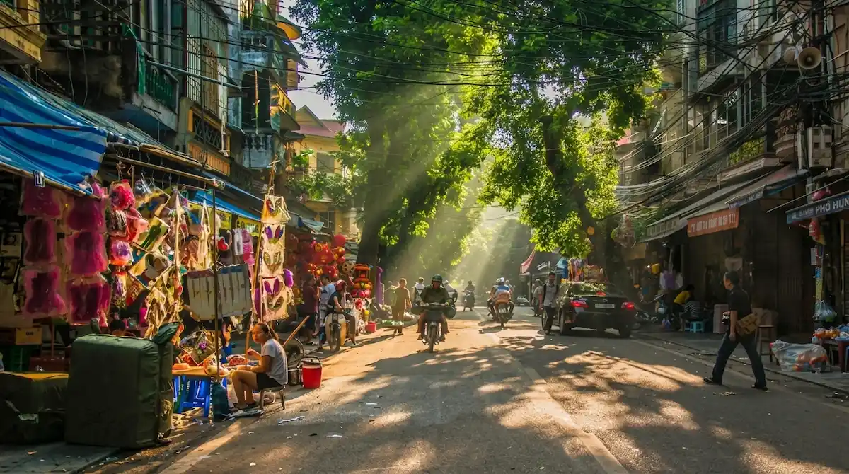 Morning Sunlight in Hanoi Old Quarter | Vietnam Discovery Tours Golden morning sunlight streaming onto a bustling street in Hanoi Old Quarter, captured during a cultural trip with Vietnam Discovery Tours.
