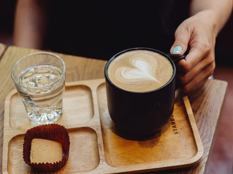 Hot Latte Art at Starbucks St. Joseph's Cathedral - Vietnam Discovery Tours A cup of hot latte with heart art, a cookie, and a glass of water on a wooden tray at Starbucks near St. Joseph's Cathedral Hanoi