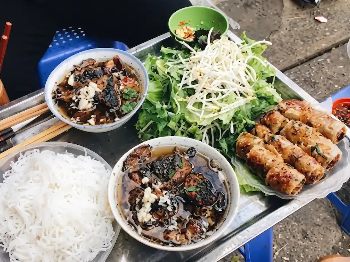 Traditional Bun Cha Hanoi Meal Set - Vietnam Discovery Tours Authentic Bun Cha combo served on a metal tray with grilled pork, crab spring rolls, and fresh herbs - Vietnam Discovery Tours